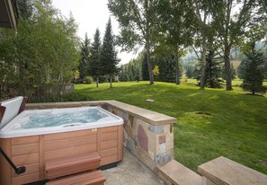 Ein Whirlpool mit Steinwänden und Holzstufen, umgeben von einem Rasen und Bäumen.