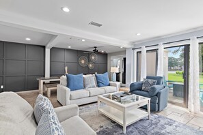 Una sala de estar moderna con un sofá gris, sillones azules, una mesa de centro y un comedor.