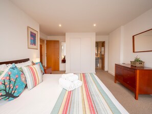 A bedroom with a bed, a bedside table, a dresser, a mirror, and a door leading to another room.
