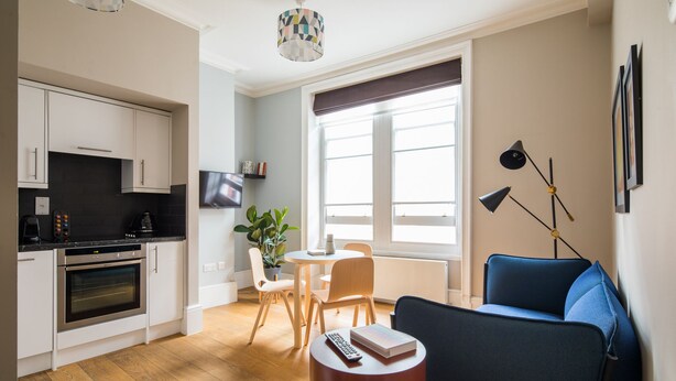 A modern kitchen with white cabinets, a built-in oven, and a dining area with a round table and chairs. - Vibrant Covent Garden 1BR - Netflix & Nespresso (London)