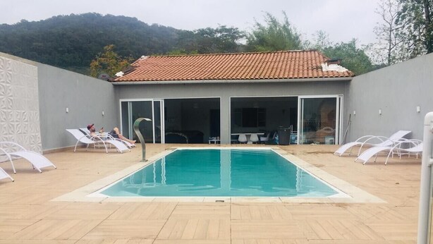 A rectangular pool with a tiled roof, surrounded by lounge chairs and a covered seating area. - House on the south coast with optional heated pool. (Mongaguá)