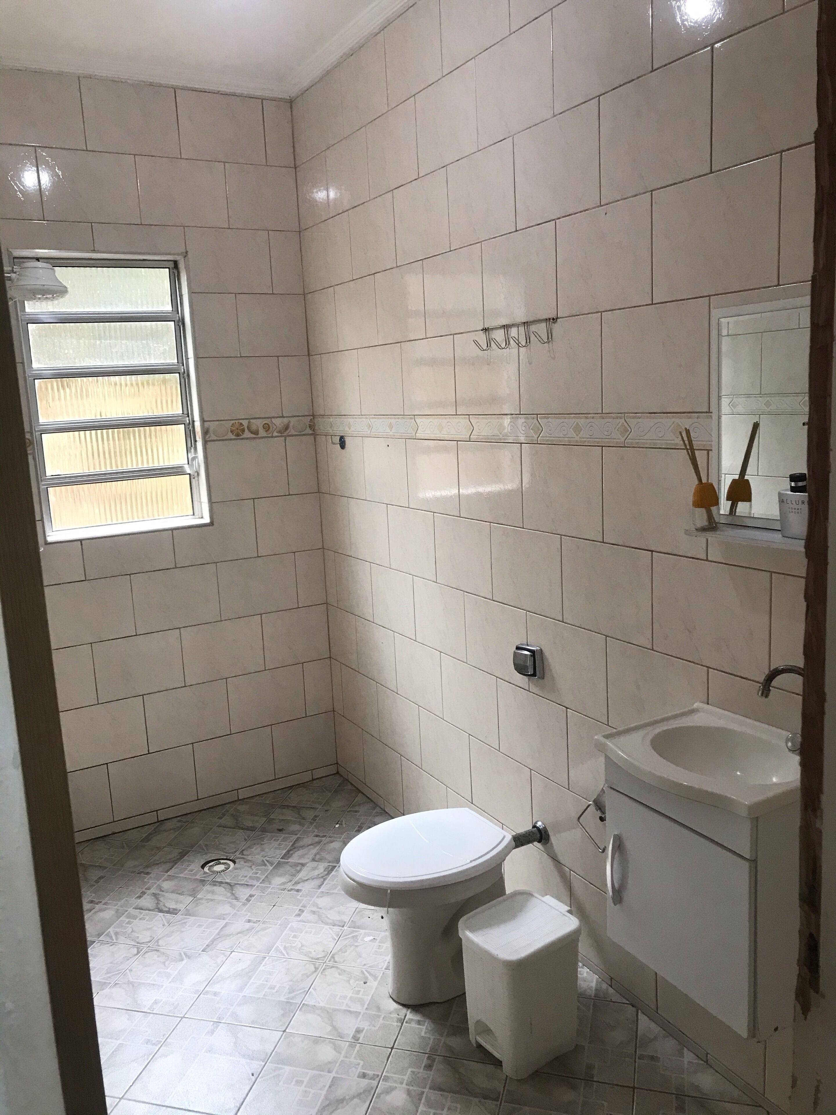 A bathroom with white tiles, a toilet, a sink, and a window.