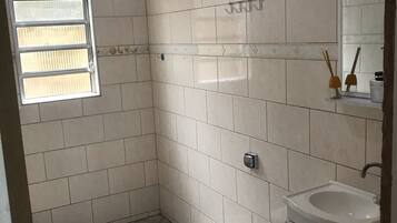 A bathroom with white tiles, a toilet, a sink, and a window.