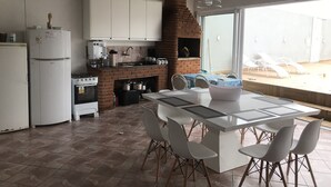A kitchen with a brick oven, white cabinets, and a dining area with a table and chairs. - House on the south coast with optional heated pool. (Mongaguá)