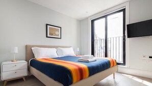 Une chambre d’hôtel moderne dotée d’un grand lit, d’une table de chevet, d’un téléviseur à écran plat et d’un balcon offrant une vue sur la ville.
