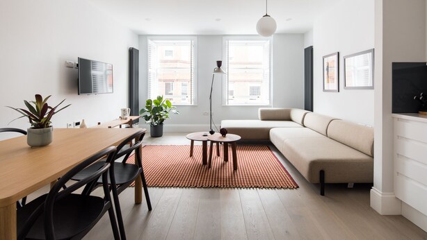 Un salon moderne avec une table à manger en bois, des chaises noires, un canapé beige et un tapis rouge.