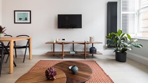 Un salon moderne avec une table à manger en bois, des chaises, un téléviseur fixé au mur, un radiateur et une plante en pot.