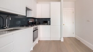 Une cuisine moderne avec des meubles blancs, un plan de travail noir, un four encastré et un micro-ondes.