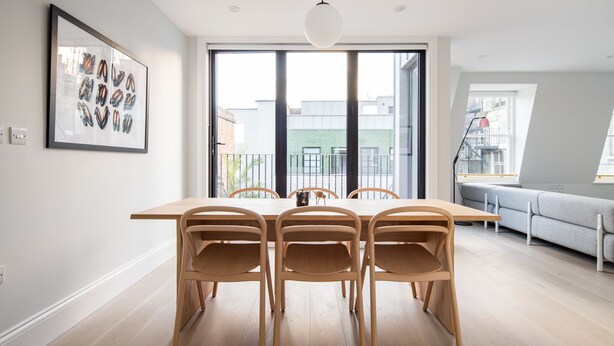 Un comedor moderno con una mesa y sillas de madera, ventanas amplias y vistas a edificios.
