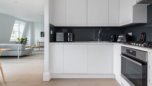 Una cocina moderna con armarios blancos, horno empotrado y cafetera.
