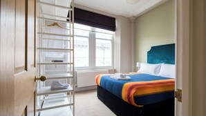 Una camera d'albergo con un letto, un armadio bianco con attaccapanni, una finestra con vista e un termosifone.