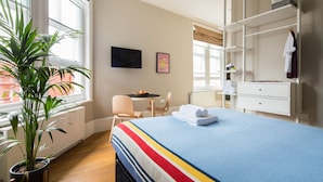 Ein Hotelzimmer mit einem Bett, einem Schreibtisch, einem Stuhl, einer Topfpflanze und einem Fenster.