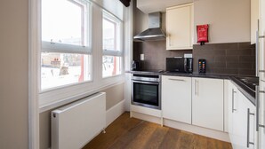 A modern kitchen with white cabinets, a built-in oven, a microwave, and a stove. There is a window providing natural light and a view of the outside. - Bright Covent Garden Studio - Netflix & Nespresso (London)