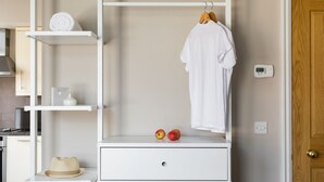 A white wardrobe with a hanging robe, two apples, and a straw hat on a shelf. - Bright Covent Garden Studio - Netflix & Nespresso (London)