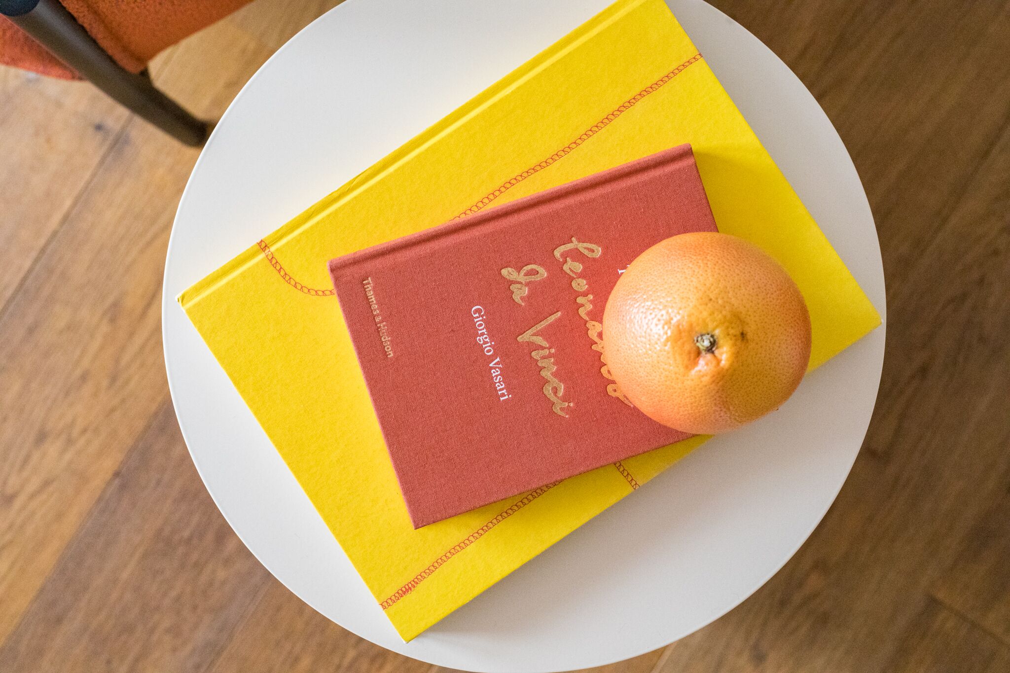 A book titled "Le voyage de Giotto Vasari" on a yellow book cover, placed on a white plate with an orange on top.