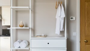 Une commode blanche à deux tiroirs, une étagère avec des serviettes enroulées et un porte-vêtements avec des robes blanches.