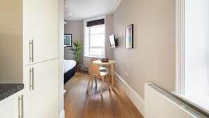 Une pièce de taille modeste comprenant un lit, une petite table à manger avec des chaises, une plante en pot et une fenêtre donnant sur un paysage agréable.