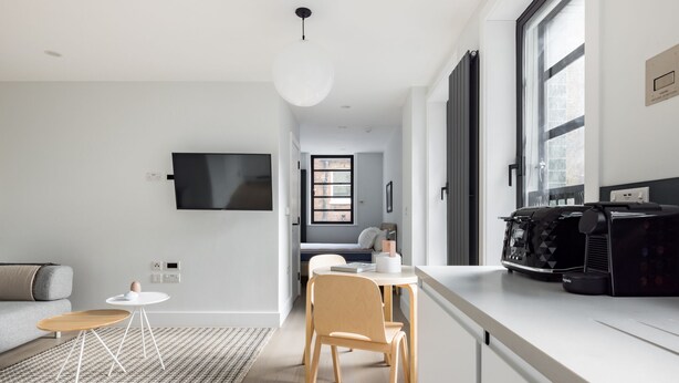 A modern kitchen with a dining area, a flat-screen TV mounted on the wall, and a coffee machine on the counter. - Calm Leicester Sq Studio - Netflix & Nespresso (London)