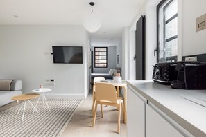 A modern kitchen with a dining area, a flat-screen TV mounted on the wall, and a coffee machine on the counter. - Calm Leicester Sq Studio - Netflix & Nespresso (London)