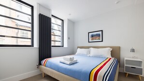 A neatly arranged bedroom with a bed, a bedside table, a window, and a picture on the wall. - Calm Leicester Sq Studio - Netflix & Nespresso (London)