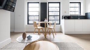 A modern kitchen with two windows, a dining area with a round table and chairs, and a TV mounted on the wall. - Calm Leicester Sq Studio - Netflix & Nespresso (London)