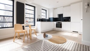 A modern kitchen with white cabinets, a black countertop, and a dining area with a round table and chairs. - Calm Leicester Sq Studio - Netflix & Nespresso (London)