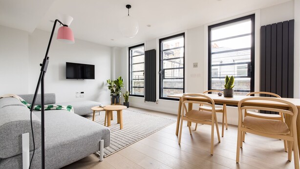 Un salon moderne avec un canapé gris, une table à manger en bois et des chaises. On y trouve également un lampadaire, un téléviseur à écran plat et une plante en pot.