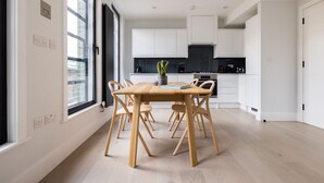 Une cuisine moderne avec des meubles blancs, une table à manger en bois et une grande fenêtre.