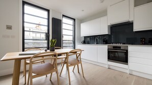Une cuisine moderne avec des meubles blancs, une table à manger en bois et deux chaises.