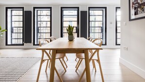 Et moderne spiseområde med et træbord og stole, store vinduer med sorte rammer og en potteplante på bordet.
