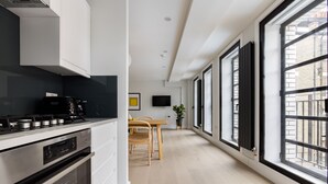 Et moderne køkken med indbygget ovn og komfur, et spiseområde med bord og stole, samt store vinduer med udsigt over byen.