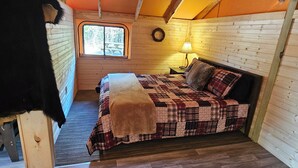 Une chambre confortable avec un lit en bois, une fenêtre, une lampe fixée au mur et une porte.
