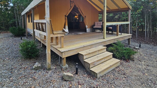 Une cabane en bois dotée d’un porche couvert, d’un petit espace extérieur aménagé pour s’asseoir et offrant une vue sur la forêt environnante.