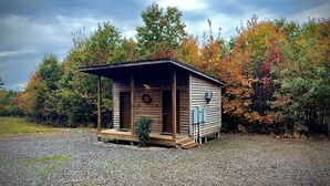 Une petite cabane en bois dotée d’un porche, entourée d’un feuillage automnal.
