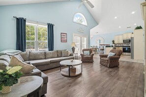 A living room with a sofa, armchairs, a coffee table, and a dining table. There is a kitchen in the background with cabinets and appliances. - Spacious Surfside Beach Home Minutes from the Ocean. Pet-Friendly! (Murrells Inlet)