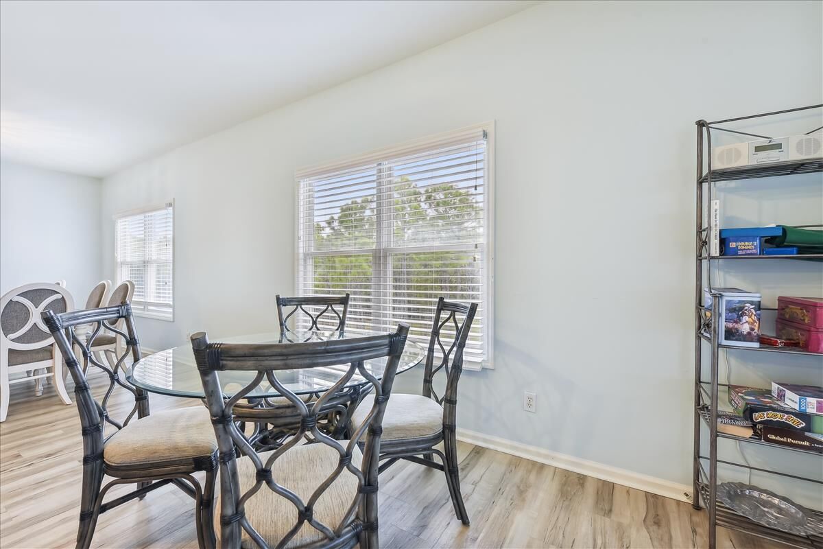A dining area with a round table and chairs, white walls, and a window with blinds.