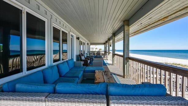 A covered outdoor seating area with blue cushioned sofas and wicker tables, overlooking a beach. - Coastal Cottage is situated on the island's east end near the State Park. (St. George Island)