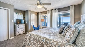 A bedroom with a bed, a ceiling fan, a dresser, a chair, and a view of the outdoors. - Coastal Cottage is situated on the island's east end near the State Park. (St. George Island)