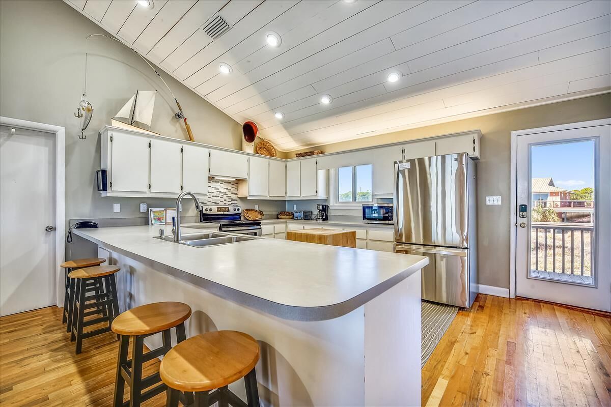 A modern kitchen with a large island, wooden stools, and a view of the outside.