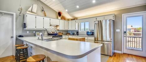 A modern kitchen with a large island, wooden stools, and a view of the outside.