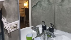 A bathroom with a white sink, green cups, and a mirror reflecting a room with a chair and a lamp.