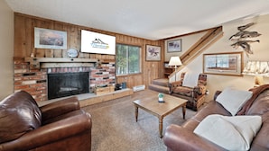 A cozy living room with a fireplace, leather sofas, a wooden staircase, and framed pictures on the walls.