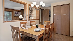 A dining room with a wooden table, chairs, a chandelier, and a large mirror.