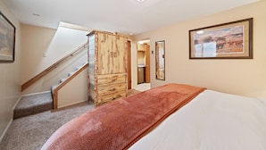 A bedroom with a bed, a wooden wardrobe, a staircase, and a framed picture on the wall.