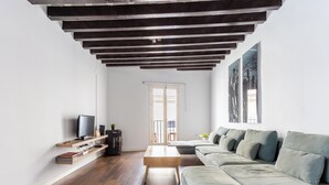Un soggiorno moderno con soffitto in legno, un divano ampio, una televisione e una libreria.