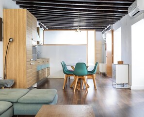A modern kitchen with wooden cabinets, a dining area with teal chairs, and a wooden dining table.