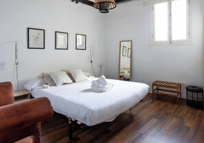 A bedroom with a bed, bedside table, chair, wooden bench, and a window with a view.