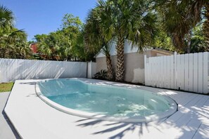 Une piscine à bordures courbes, entourée d’une terrasse blanche et d’une clôture blanche.