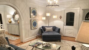 Un salon avec un canapé bleu, une table basse en verre et un lustre.