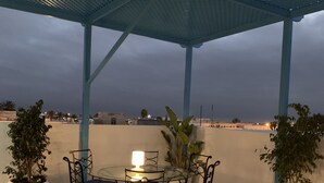 A covered patio with a table and chairs, potted plants, and a view of the cityscape. - Dar Lola, guest house in the medina (Houmt Souk)